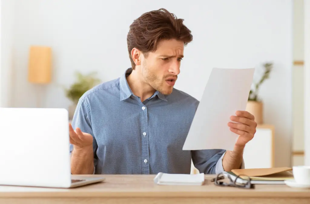 Mann sitzt fassungslos vor seinem Laptop und hält ein Dokument in der Hand – zeigt Unsicherheit über Ansprüche oder Leistungen der Arbeitslosenversicherung Schweiz.