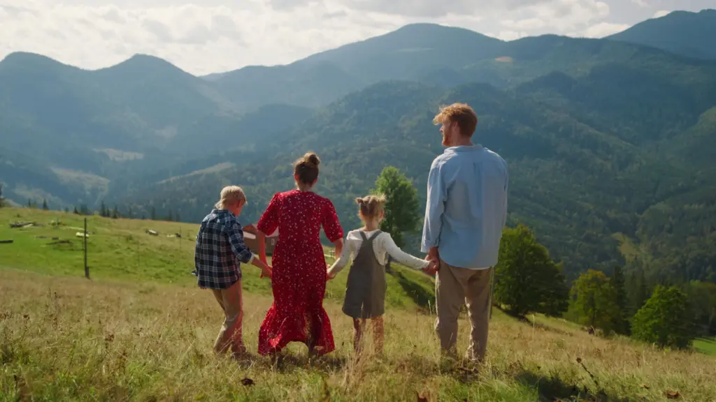 Familie mit zwei Kindern steht Hand in Hand auf einer Wiese und blickt in eine Berglandschaft – sinnbildlich für einen gelungenen Familiennachzug Schweiz und ein neues gemeinsames Leben.