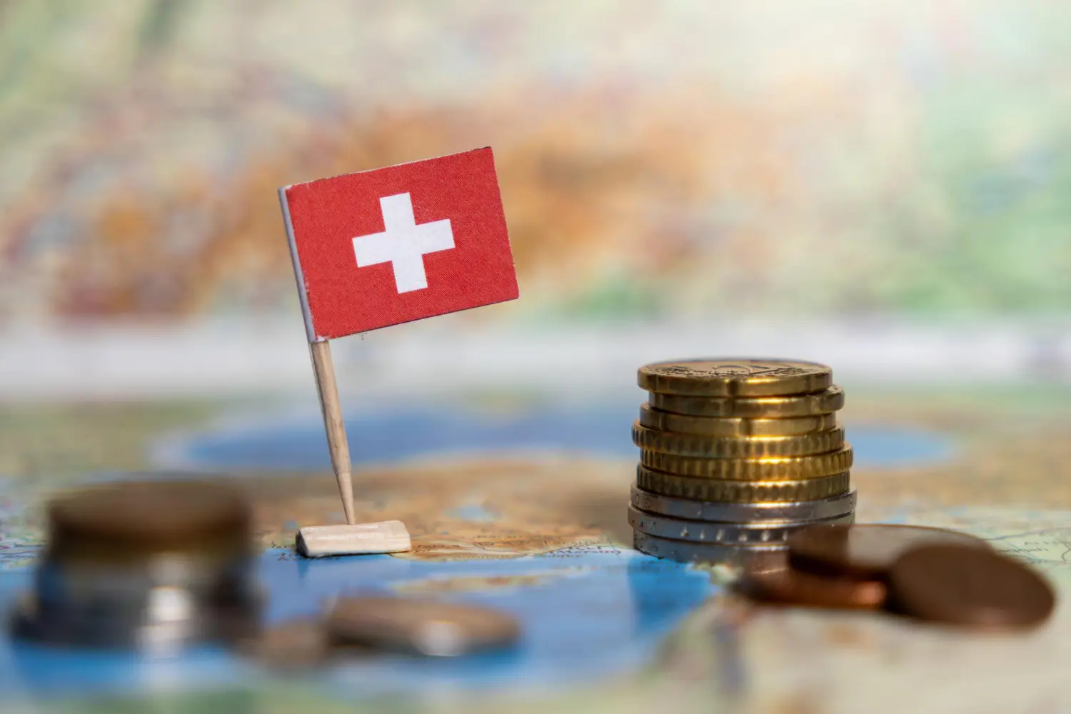 Kleine Schweizer Flagge steckt auf einer Landkarte neben aufgestapelten Münzen – sinnbildlich für wirtschaftliche Aspekte und Lohnniveau im Kontext der Arbeitsbedingungen Schweiz.